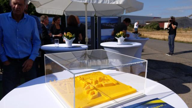 Ein 3D Druck der Gebäude auf einem Tisch dahinter Ausstellungswände, Sonnenschirme, Stehtische und freies Feld
