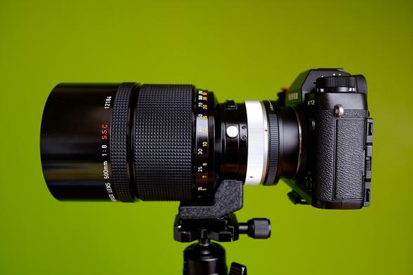 Side view of a camera with a large lens in front of a green wall.