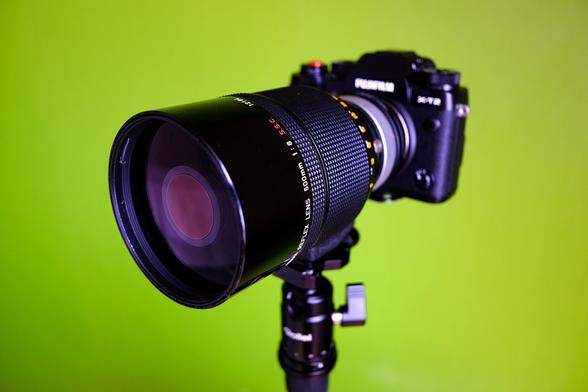 A camera with a large lens in front of a green wall.