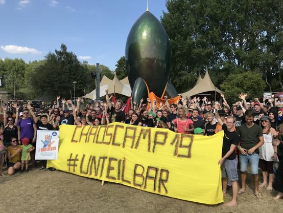 Menschen jubelnd vor Rakete mit Transpi "Chaoscamp 19 #unteilbar"