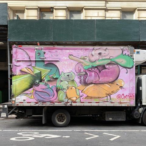 The entirety of the side of a box truck has been covered in a graffiti mural with pink background and many fantastical animals. It has been signed "@cernesto"