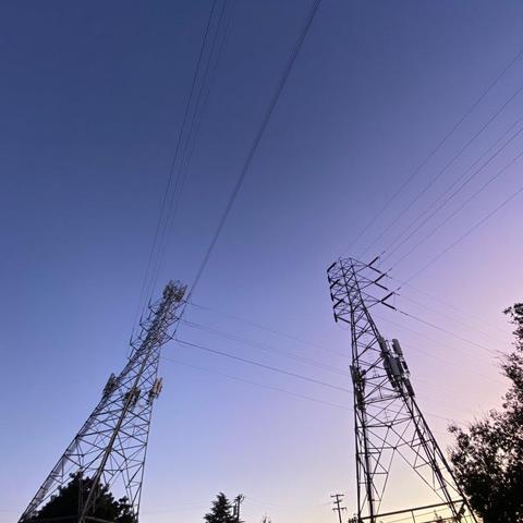 Two electrical towers loom overhead with a clear sunset sky behind them