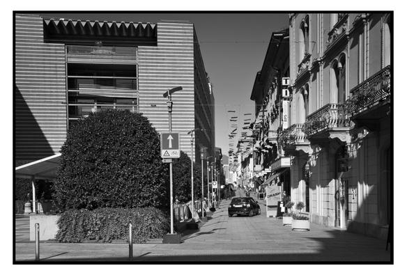 A Mini[Maxi?] drives on a paved street, which the sign seems to indicate is restricted to bicycles, and turns right just past a street hording which is shouting "CRASH".

A monochrome: taken in the small Border Town of Chiasso, Switzerland.

This image is rendered as Ilford-FP4-125-ISO and presented in the style of: mounted on a black-board which in turn is mounted on a white-board.