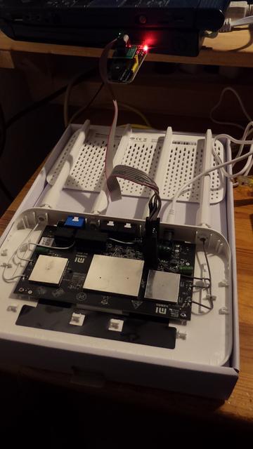 WiFi Router with opened case still sitting in it's original packaging. A chip-clamp and cables are attached to components inside the router and connected to a laptop.
