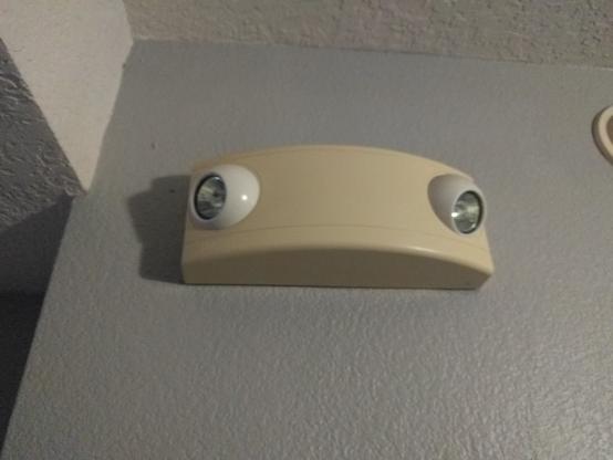 An emergency light has two bulbs pointing 90 degrees apart on a curved face.