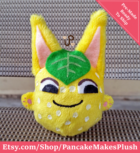 A palm-sized plush of Tangy from Animal Crossing. She's a little yellow-orange orb with big ears and little hands poking out the sides. She's got white spots and a green leaf on her head.