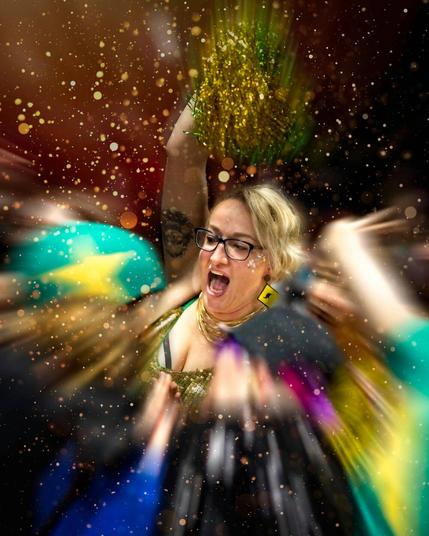 A fan cheering, one green-gold cheerleader pom-pom up in the air. Players and other fans around are blurred by a zoom-in effect, gold sparks are everywhere emphasizing the celebration.