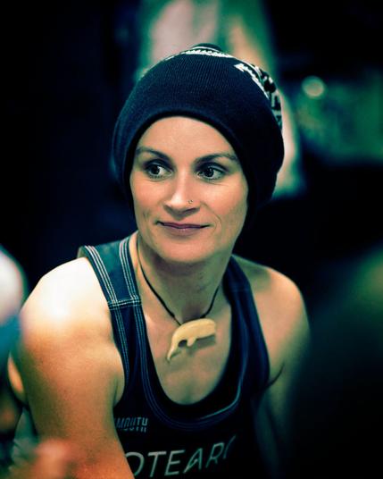 Low-key colour picture of a spectator at a sports event. Beanie hat and tank top with a bone whale surfer necklace. Lightly smiling and eyes focussed in the void.