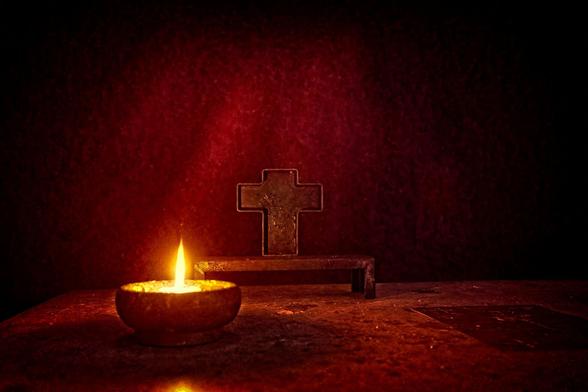 Dark, reddish picture of a candle and a cross on top of a modern altar in Notre-Dame-du-Haut in Ronchamps, the famous church built by Le Corbusier.