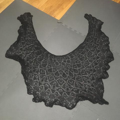 Black knit lace shawl scattered with red beads. It is unblocked and looks like a blob.