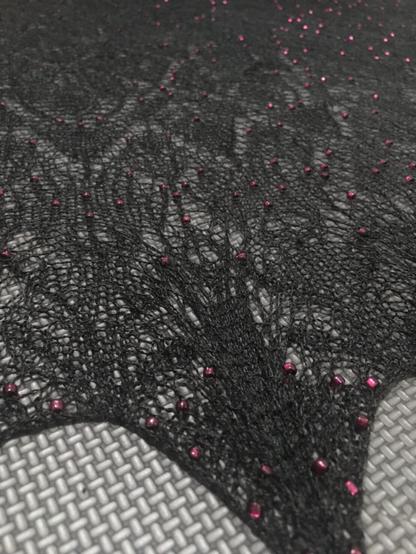 A close up of a black knit lace shawl. It is scattered with red beads.