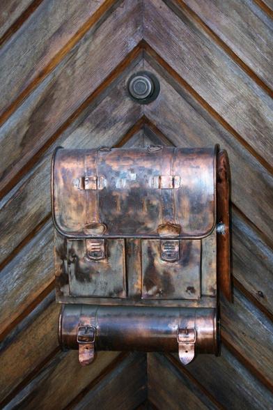 A bronze satchel on a wooden door. It serves as a nameplate.