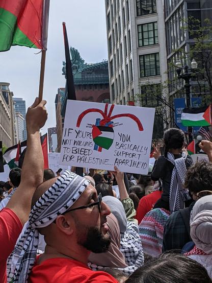 A marcher holds a sign with an anatomical drawing of a heart with its valves. The heart is colored in with the Palestinian flag and the sign reads "If you're not willing to bleed for Palestine, you basically support Apartheid"