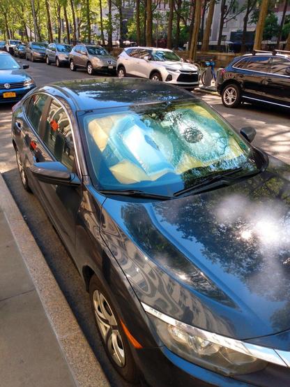 A parked car with a Minion windshield sunshade in the window. The sunshade consists of the Minion's eyes.