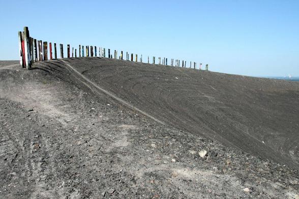 Many equidistant colourful stakes at the top left of the image towards the horizont. Gravelly ground and a steep descent all over the place.