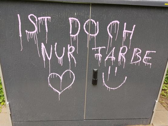 A grey cable box you usually see on the streets where are internet distribution or other infrastructure is inside showing a sprayed "Ist doch nur Farbe" (It's just only paint) followed by a heart and a upright smiley - this one: =)