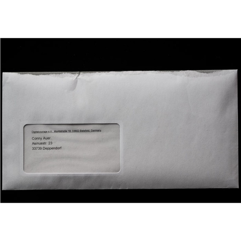 Ein weißer DIN-Fensterumschlag. Die obere Kante ist so bedruckt, dass sie beim ersten aus-dem-Briefkasten-fischen auf die Schnelle so aussieht, als wäre sie bereits aufgerissen worden.