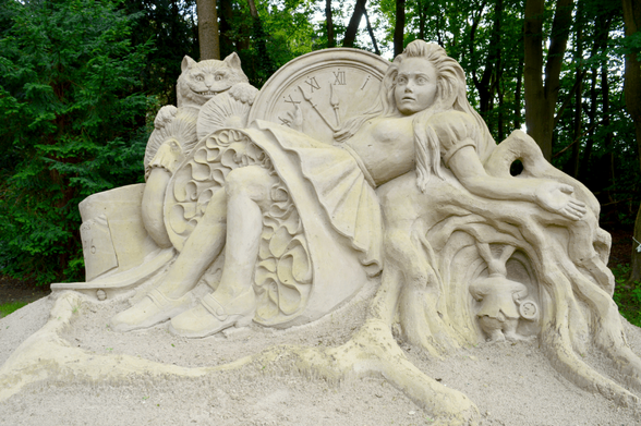 A sand sculpture of Alice in Wonderland, showing Alice lying in between a clock and a rabbit hole. Behind the clock in the Cheshire Cat.