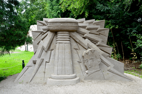 A sand sculpture of Nikola Tesla next to a transmission tower.