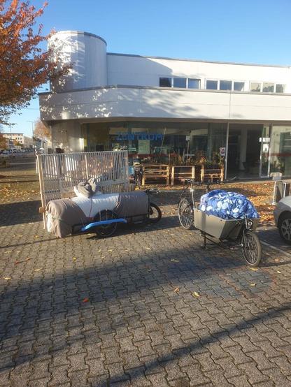 Ein Lastenrad mit Anhänger steht vor dem WandelWerk. Auf dem Anhänger ist eine Matratze und ein Lattenrost, im Lastenrad sieht man Bettwäsche.