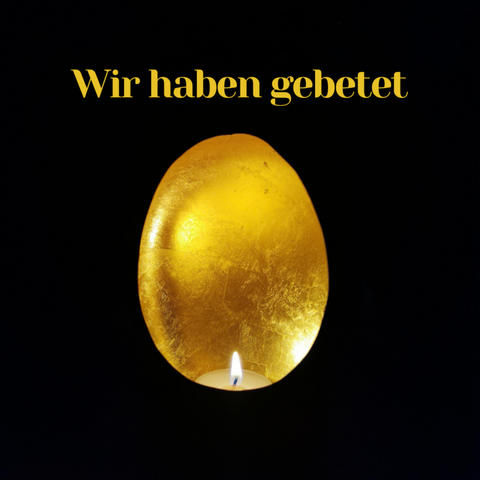 Ein Teelicht in einer Eieförmigen, goldfarben erleuchteten Schale. Der Hintergrund ist vollständig dunkel. Über dem Licht steht in gelber Schrift: "Wir haben gebetet".