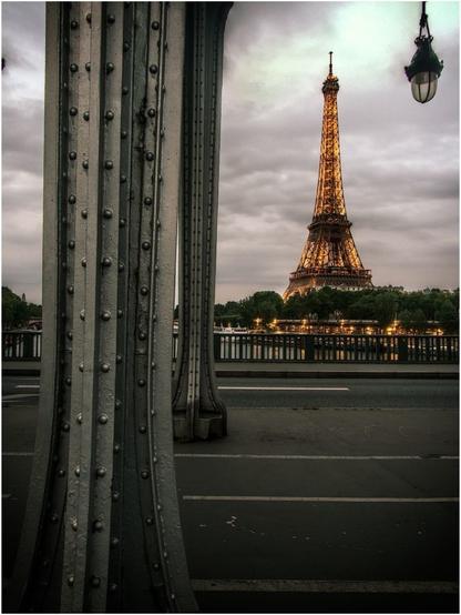 Paris. La tour Eiffel est en arrière-plan, sur un ciel nuageux de fin d'après-midi.
La photo est prise depuis la passerelle de Bir-Hakeim (pont enjambant la Seine), au milieu du tablier routier et piétonnier.
On voit apparaitre, sur la gauche de l'image, deux piles métalliques avec leurs rivets. Elles portent le tablier ferroviaire supérieur (non apparent sur la photo).
En-haut à droite de l'image, un lampadaire semble suspendu au ciel.
