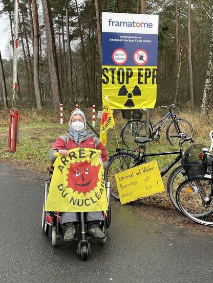 Person im Rollstuhl mit fahne "Arrêt du nucléaire" hinten Schilf mit Framatome 7nd darunter Fahne stop EPR