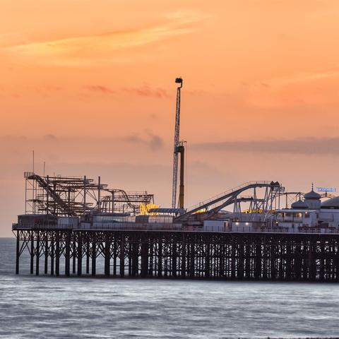 The end of brighton pier at sunset, with a orange sky, and misty water (due to image stacking). The big dipper is at its highest point.