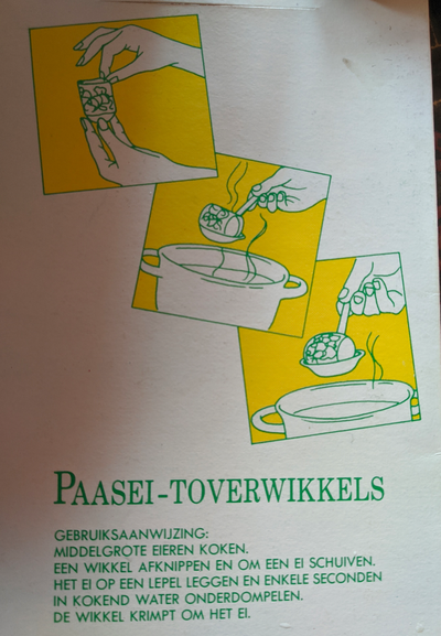 Backside of the package of Easter Egg Magic Wraps.
Three instructional drawings showing how to put a wrap around an egg, dip it into hot water while on a spoon, and lift it out again with the wrap wrapped tightly around the egg.
Below it are the instructions written in Dutch.