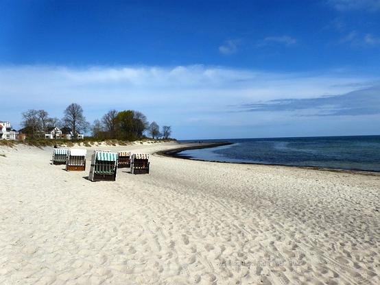 The sandy beach at Boltenhagen with wicker beach chairs. Sky and sea are blue with some cloud in the distance.