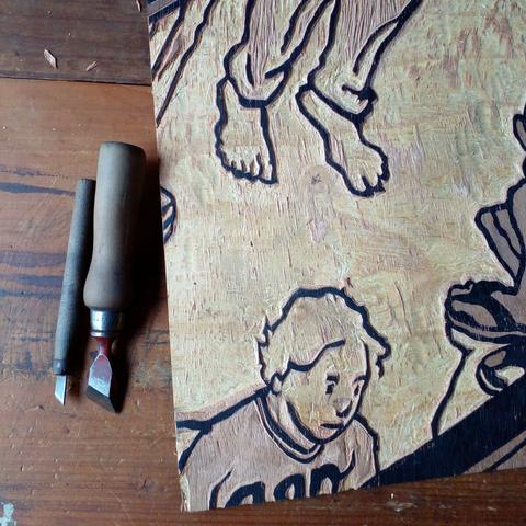 wip: a photograph picture showing a woodcut board and two carving knives seen on a table from above.
