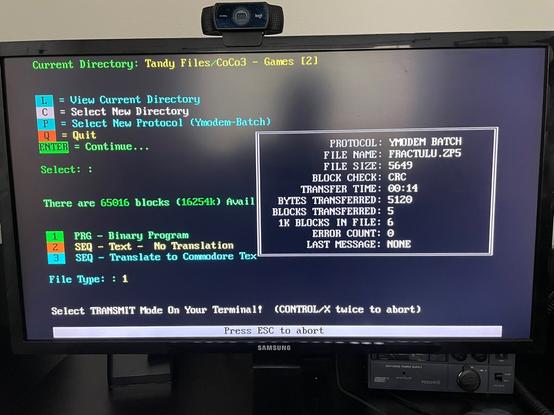 A picture of a terminal session is on a Samsung LCD display.  The top of the image says "Current Directory: Tandy Files/CoCo3
- Games [2]".  The "dialog" box indicates that the YModem transfer protocol is being used to send FRACTUL.ZP5, a file that is 5,694 bytes.  At 5,120 bytes transferred this implies the photo was taken during the file transfer.