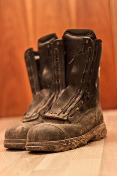 Ein paar dreckige Haix Feuerwehrstiefel auf Holzboden. Hintergrund eine Holztür.