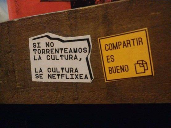 Dos stickers, uno dice "si no torrenteamos la cultura, la cultura se netflixea", el otro dice "compartir es bueno"