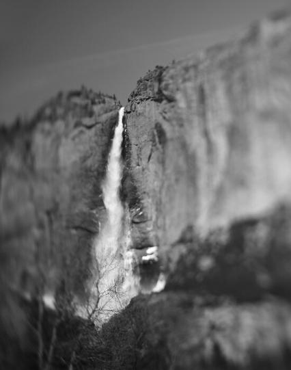 black and white digital photo of waterfall in yosemite valley. looking up from ground view at the very big waterfall. the waterfall is the only thing in focus in this tilt-shift photograph.