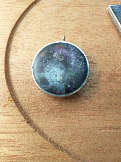 A circular galaxy pendant on a wooden platter.