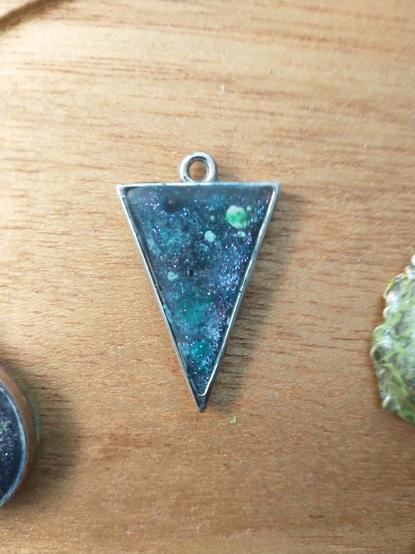 An upside down triangle pendant with planets and stars on a wooden platter.
