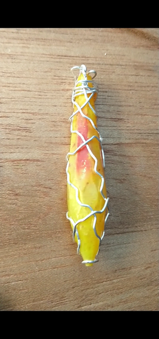 A wooden platter filled with pendants, in the center a crystal shaped yellow pendant with a red orange center highlight and silver wire wrapped around it.