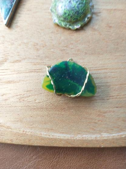 A crescent shaped pendant wrapped with gold wire and colored with yellow and green blooming in the center.