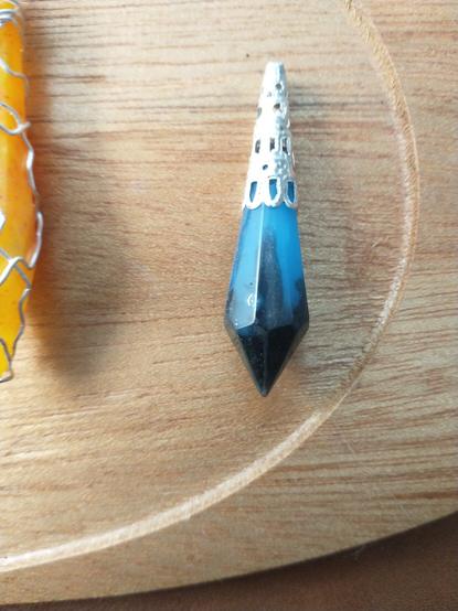 A black and blue pendant with a silver cap on its top on a wooden platter.