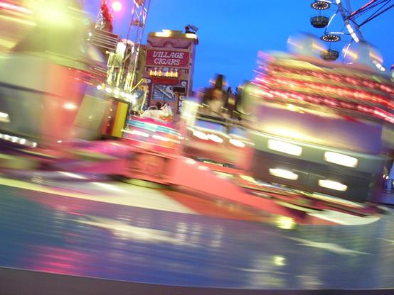 Abends schwirren die Gondeln des Fahrgeschäftes "Sound Machine" mit eingeschalteten Lichtern am Außenstehenden vorbei.