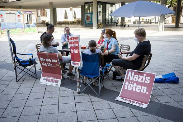 Der antifaschistische Gegenprotest der Partei DIE PARTEI hat es sich auf Stühlen im Schatten bequem gemacht.