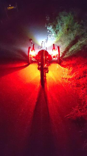 A rather low KMX recumbent trike from the back with four bright LED lights, two on the handle bar and two in the back of the backrest.