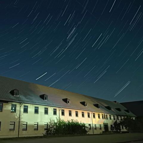 Nachtaufnahme. Angeleuchtetes Gebäude,  darüber Sternenspuren durch eine Langzeitbeluchtung.