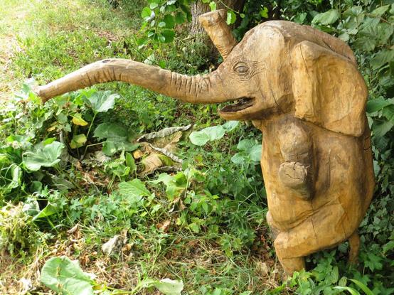Ein Foto von einer hölzernen Skulptur: Ein kleiner Elefant im Profil mit einem langen Russel und geöffnetem Maul