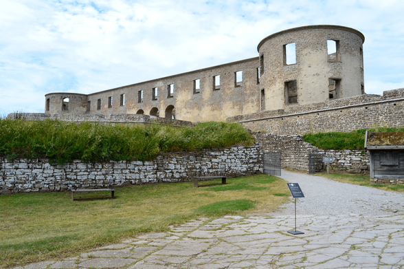 The exterior of Borgholm Castle photographed from below, outside the sort of defensive wall. A path is leading up to the ruin and in front of the wall are a few benches.