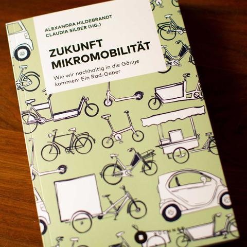 Foto des Buches "Zukunft Mikromobilität – Wie wir nachhaltig in die Gänge kommen: Ein Rad-Geber" von den Herausgeberinnen Alexandra Hildebrandt und Claudia Silber. Auf dem hellgrünen Titel sind eine Vielzahl an Fahrrädern zu sehen: Rennräder, Stadträder, Lastenräder, Pedelecs, Klapp- und Falträder sowie Roller, Lieferwagen, Kleinwagen.