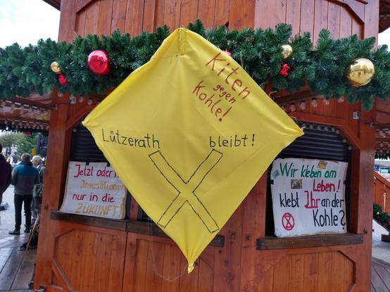 Ein Drache aus gelbem Stoff an Weihnachtsmarktbude: Aufschrift "Kiten gegen Kohle! Lützerath bleibt"