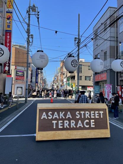 Sign reads Asaka Street Terrace in front of a busy blocked off street.