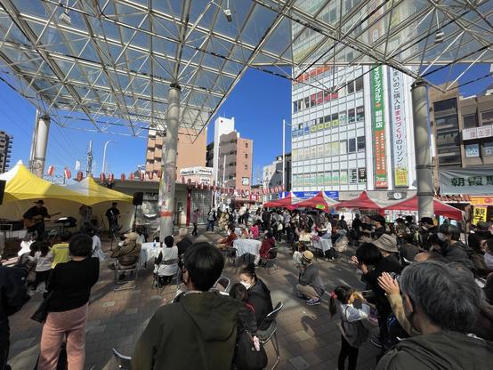 A large crowd watches a band performing in the plaza of a train station